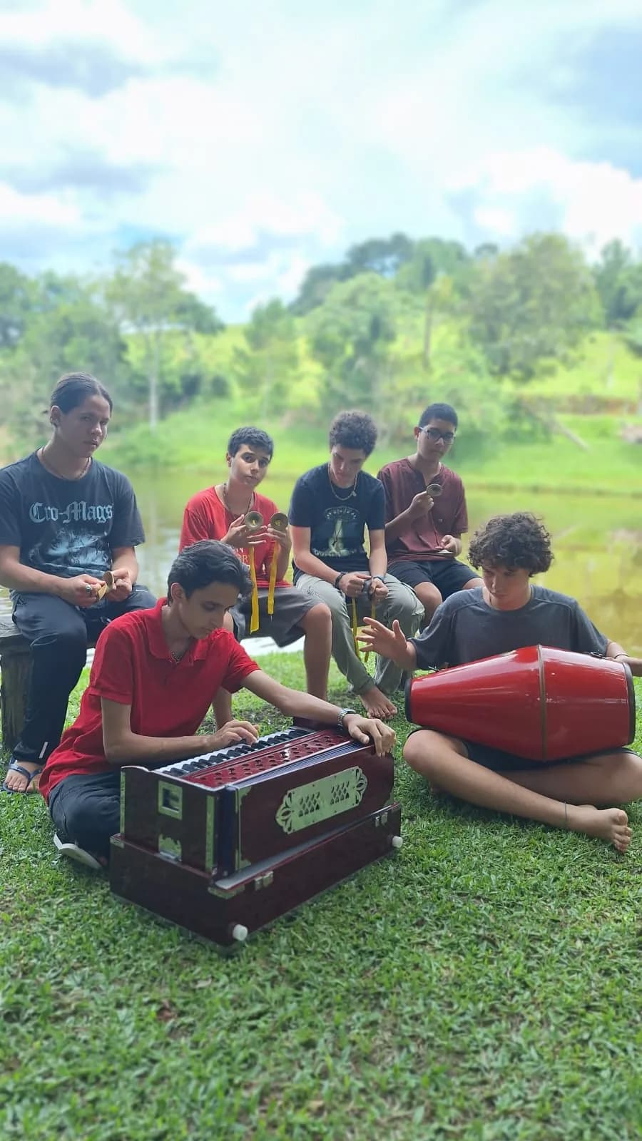 Adolescentes tocando harmônio e mridanga durante um kirtan à beira do rio